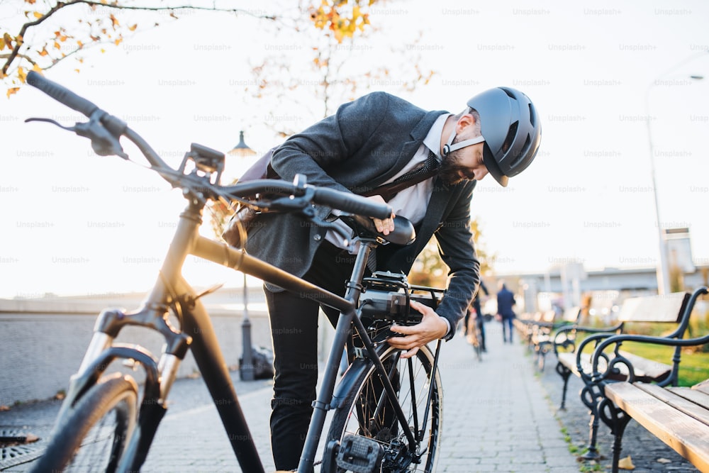 Hipster businessman commuter setting up electric bicycle when traveling home from work in city.