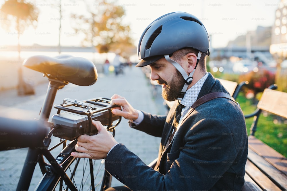 Hipster businessman commuter setting up electric bicycle when traveling home from work in city.