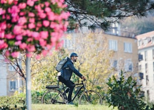 A side view of hipster businessman commuter with bicycle traveling to work in city.