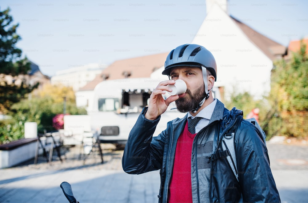 Businessman commuter with bicycle helmet going home from work in city, drinking coffee.