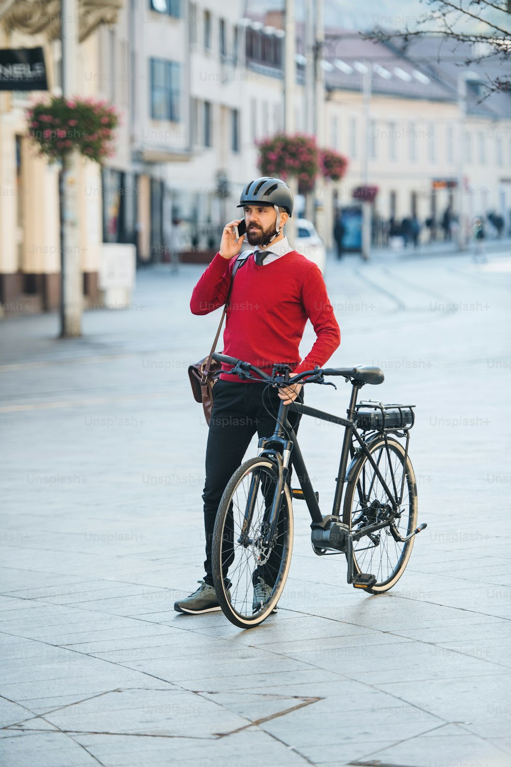 Empresário hipster se desloca com bicicleta a caminho do trabalho na cidade, em pé e usando smartphone.