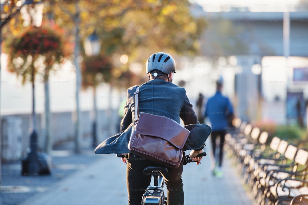 Uma visão traseira de um empresário com bicicleta elétrica viajando para o trabalho na cidade. Espaço de cópia.