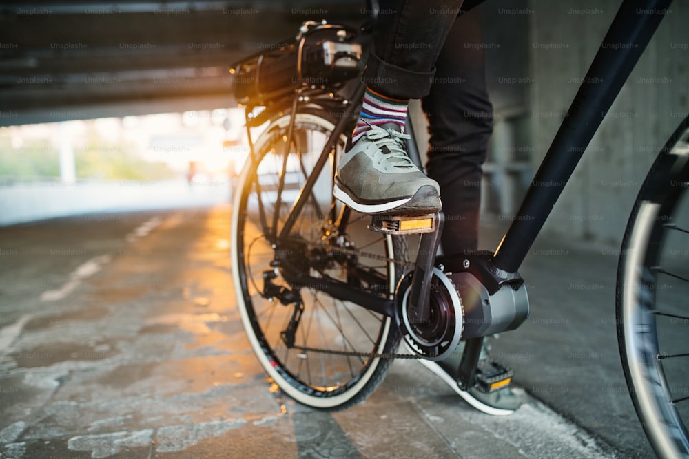 Meio-fio de empresário irreconhecível com bicicleta elétrica viajando do trabalho na cidade. Espaço de cópia.