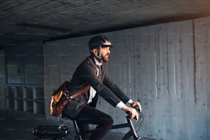 A side view of hipster businessman commuter with electric bicycle traveling to work in city. Copy space.