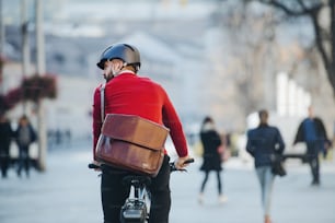 Una vista posteriore di un pendolare uomo d'affari con bicicletta elettrica che viaggia per lavorare in città. Copia spazio.