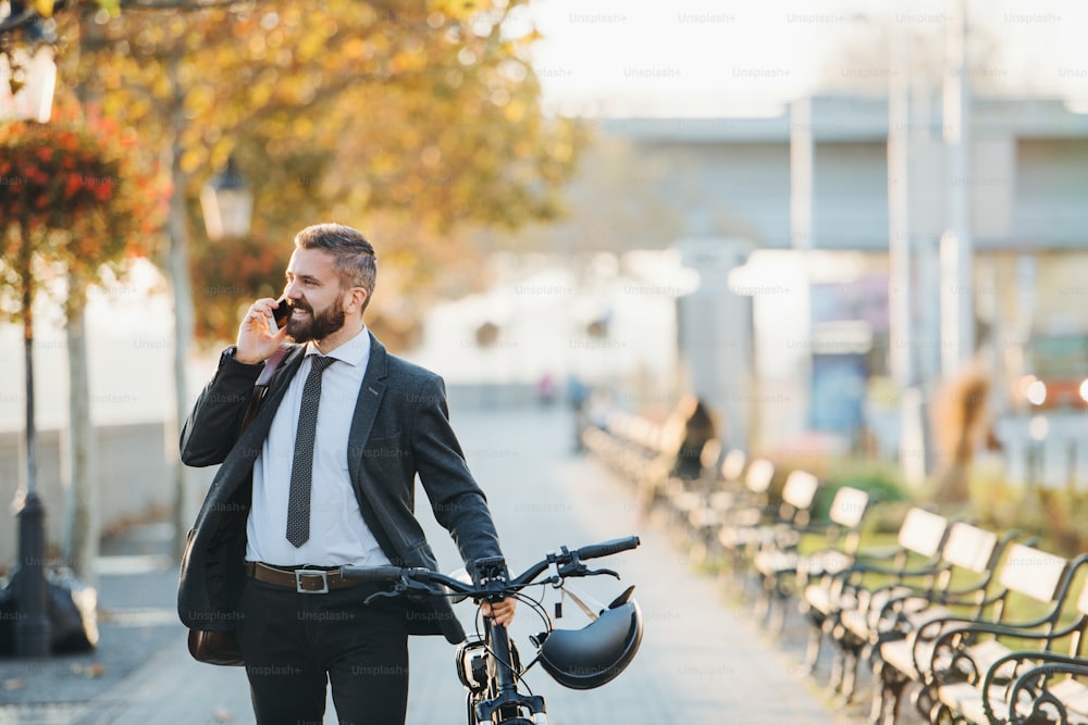 Um empresário que viaja de bicicleta caminhando para casa do trabalho na cidade, usando smartphone.