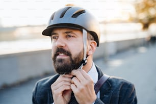 Hipster businessman commuter putting on a bicycle helmet when traveling home from work in city.