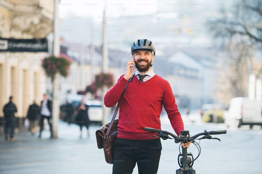 Homme d’affaires hipster banlieusard avec vélo sur le chemin du travail en ville, debout et utilisant un smartphone.