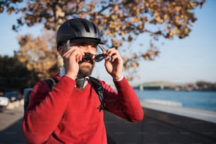 Hombre de negocios hipster con casco de bicicleta de camino al trabajo en la ciudad, poniéndose gafas de sol.