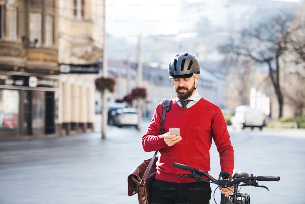 Hombre de negocios hipster viajero con bicicleta en el camino al trabajo en la ciudad, de pie y usando el teléfono inteligente.