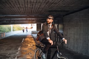 Uma vista frontal do empresário hipster com bicicleta elétrica viajando para o trabalho na cidade. Espaço de cópia.