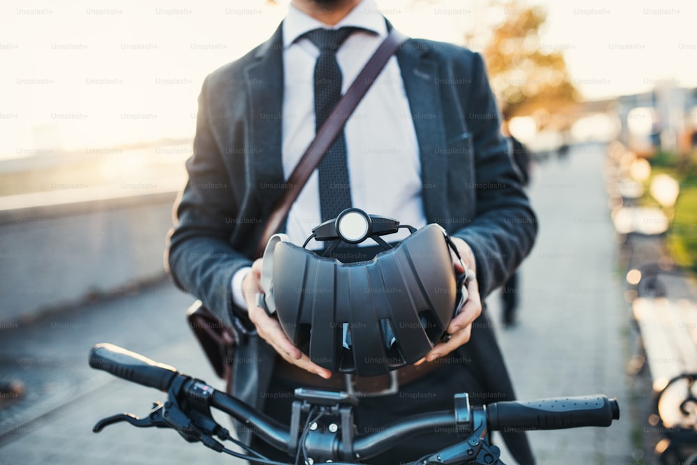 Meio-dia de empresário com bicicleta elétrica viajando para casa do trabalho na cidade, segurando um capacete.