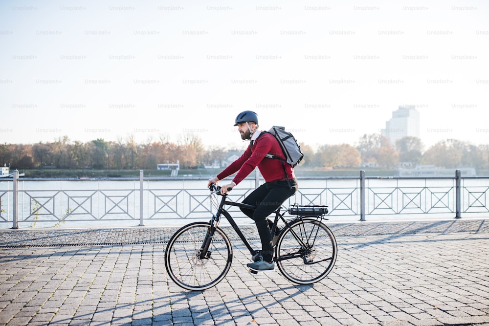 Una vista laterale del pendolare hipster uomo d'affari con la bicicletta elettrica che viaggia per lavorare in città. Copia spazio.