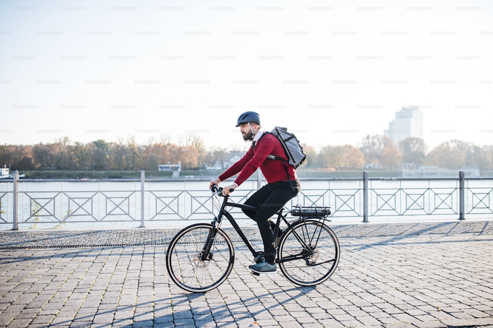 A side view of hipster businessman commuter with electric bicycle traveling to work in city. Copy space.