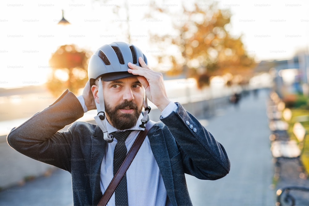 Hipster businessman commuter putting on a bicycle helmet when traveling home from work in city.