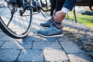 Sección media de viajero de negocios con bicicleta eléctrica que viaja desde el trabajo en la ciudad, atando zapatos.