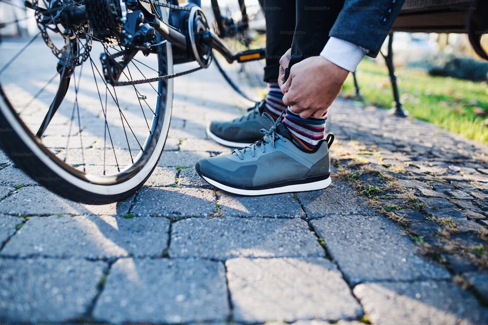 Sección media de viajero de negocios con bicicleta eléctrica que viaja desde el trabajo en la ciudad, atando zapatos.