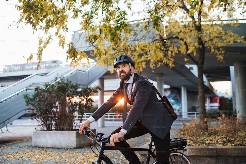 Pendolare uomo d'affari hipster con bicicletta elettrica che torna a casa dal lavoro in città al tramonto. Copia spazio.