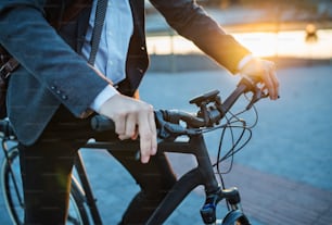 Midsection of businessman commuter with electric bicycle traveling home from work in city.