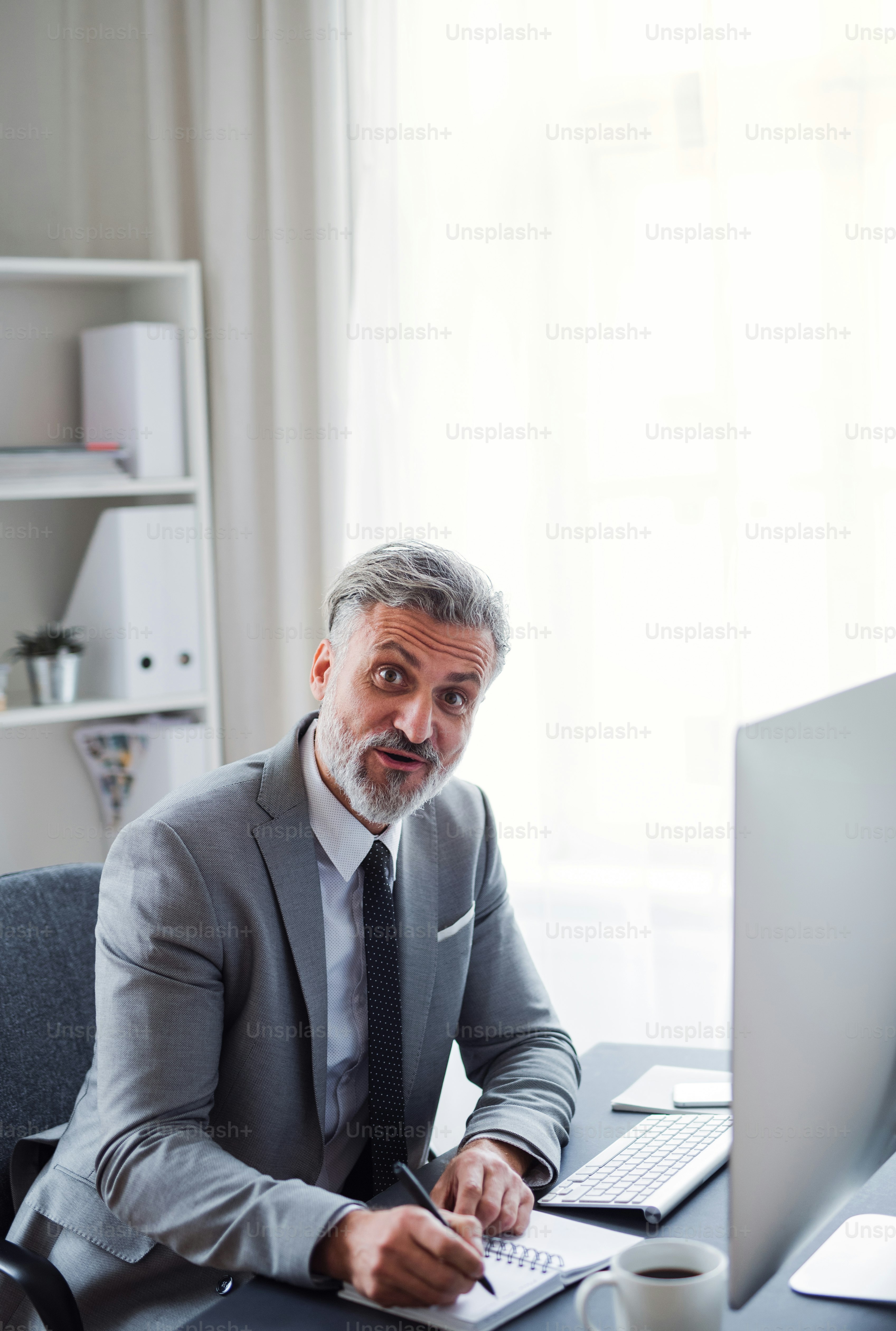 A businessman with desktop computer sitting at the table in an office, making notes