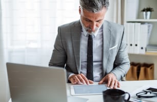 A mature businessman sitting at the table, using tablet. Copy space.