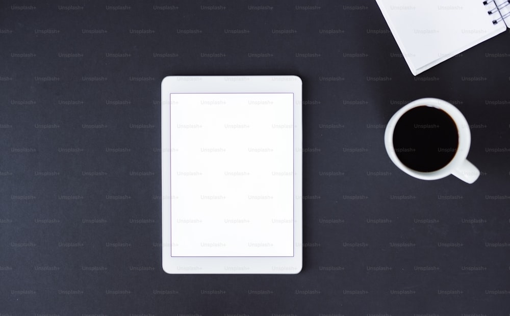 A studio shot of tablet, notepad and coffee on a black background. A top view. Copy space.