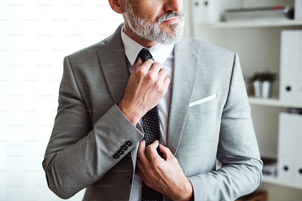 A midsection of unrecognizable mature businessman standing in an office, holding a tie.