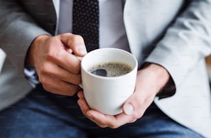 Ein Geschäftsmann, der in einem Büro sitzt und eine Tasse Kaffee in der Hand hält. Eine Nahaufnahme.