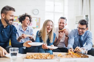 Grupo de jovens homens e mulheres de negócios com pizza almoçando em um escritório moderno.