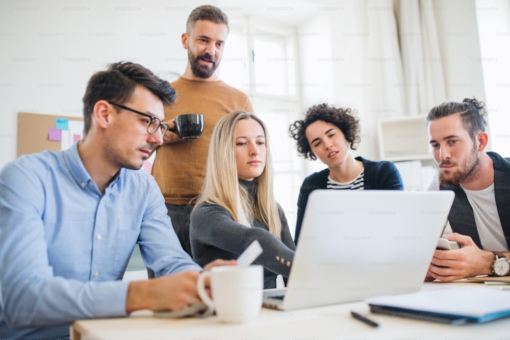 Gruppe von jungen, fröhlichen, männlichen und weiblichen Geschäftsleuten mit Laptop, die in einem modernen Büro zusammenarbeiten.