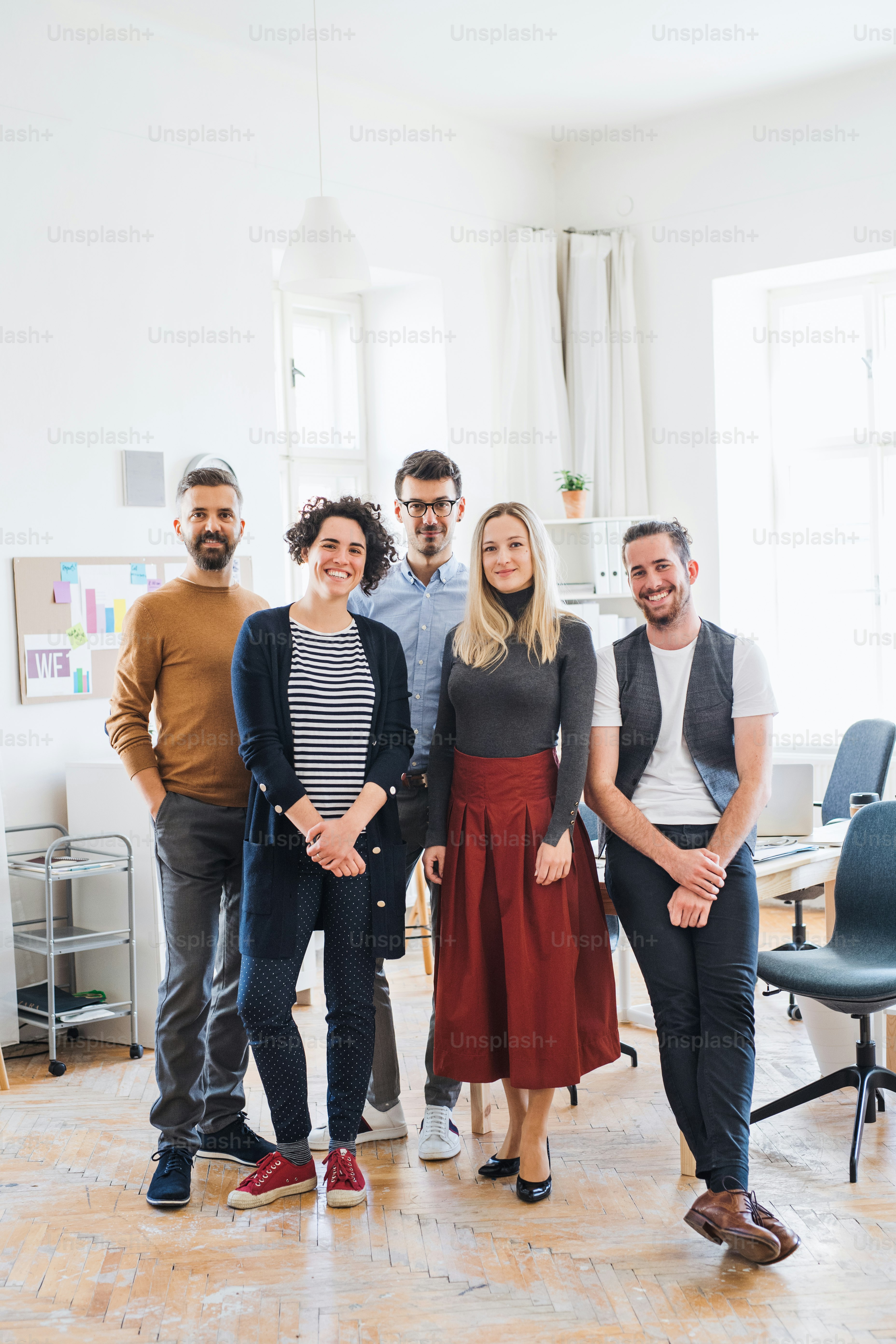 Um retrato de corpo inteiro de um grupo de jovens empresários em pé em um escritório moderno, olhando para a câmera.