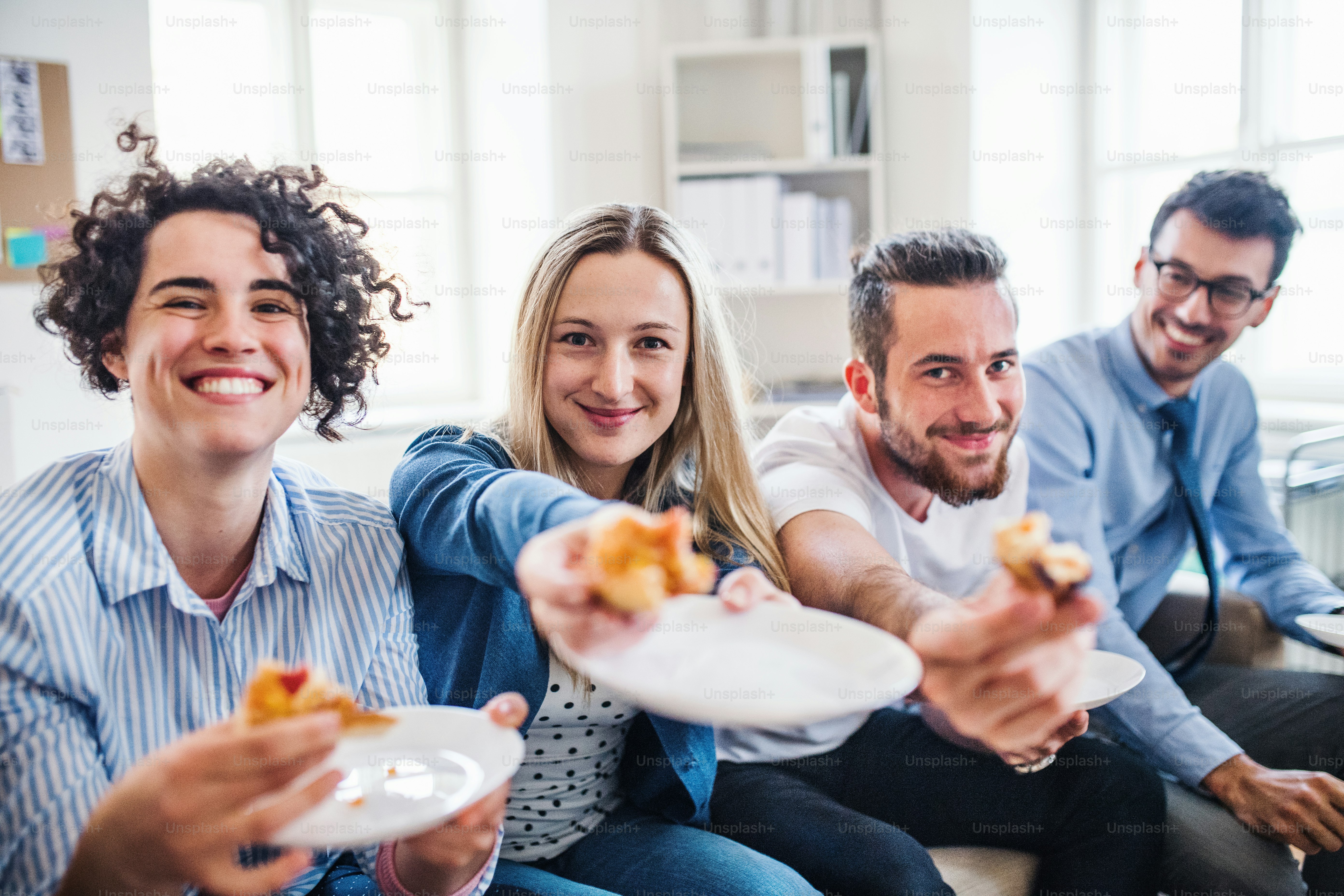 Group of young male and female businesspeople with pizza having lunch in a modern office.