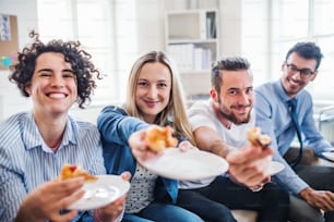 Group of young male and female businesspeople with pizza having lunch in a modern office.