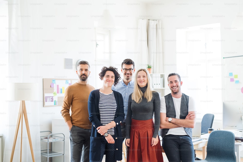 A portrait of group of young businesspeople standing in a modern office, looking at camera.