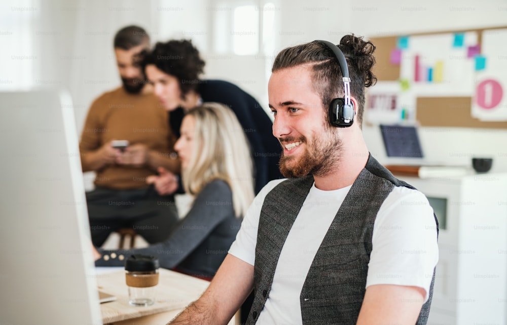Um retrato de um jovem empresário hipster com fones de ouvido e colegas em um escritório moderno, rindo.