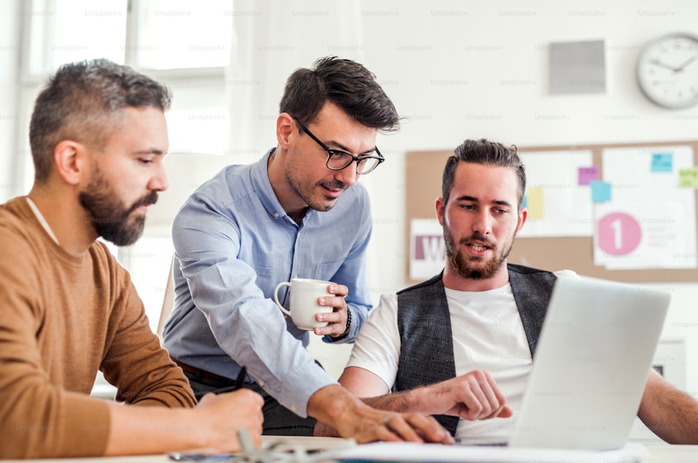 Gruppo di giovani uomini d'affari allegri con computer portatile che lavorano in un ufficio moderno.