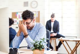 Young frustrated businessman with smartphone working in a modern office, making a phone call.