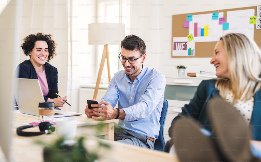 Grupo de empresários jovens, alegres, homens e mulheres com smartphone trabalhando juntos em um escritório moderno, pés sobre a mesa.