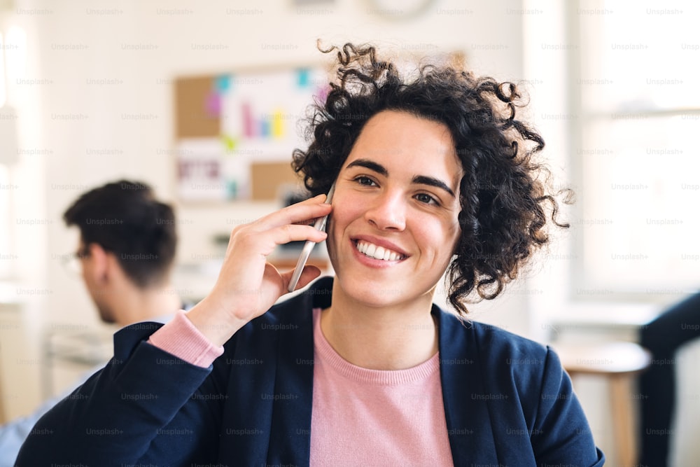 Ein Porträt einer jungen Geschäftsfrau mit Smartphone in einem modernen Büro, die telefoniert.
