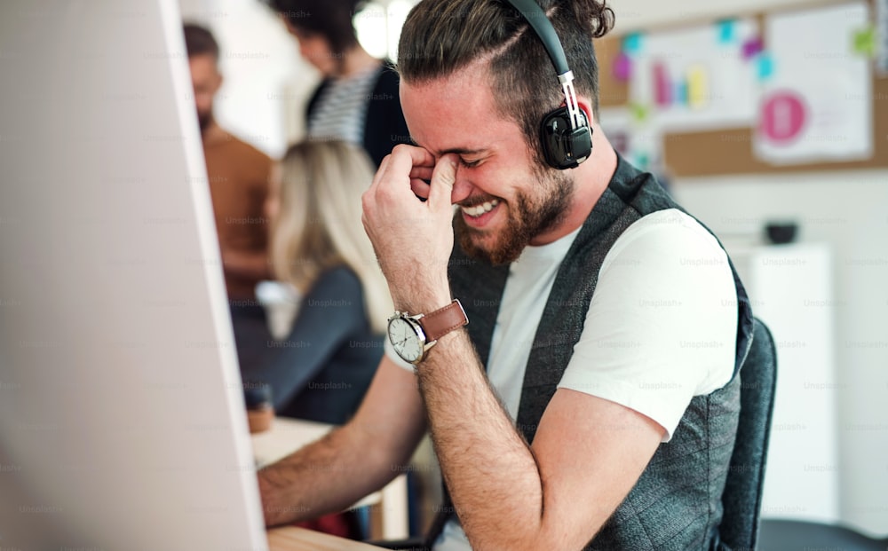 헤드폰을 끼고 있는 젊은 힙스터 사업가와 동료들이 현대적인 사무실에서 웃고 있는 초상화.