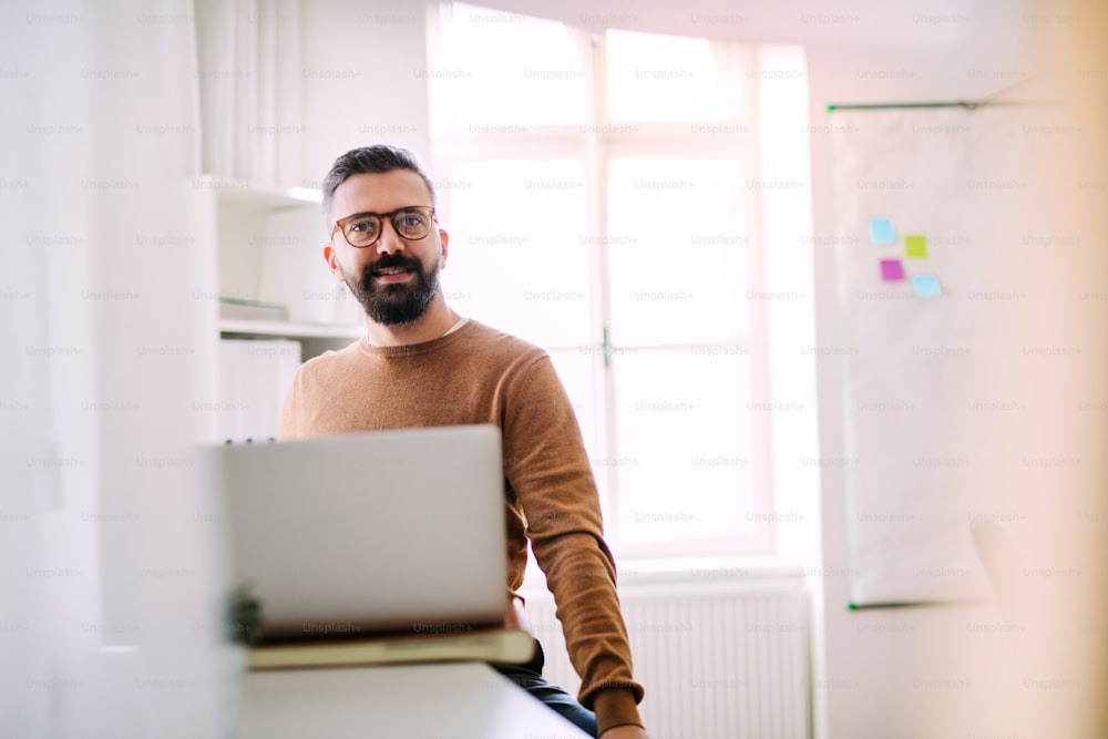 Mature hipster businessman with laptop working in a modern office. Copy space.