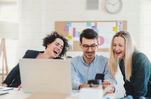 Grupo de jóvenes y alegres, hombres y mujeres de negocios con computadora portátil trabajando juntos en una oficina moderna.