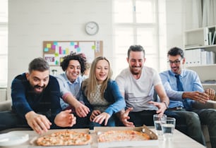 Group of young male and female businesspeople with pizza having lunch in a modern office.