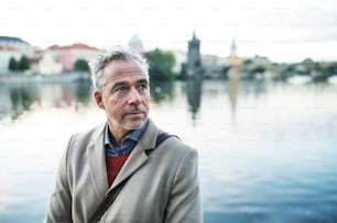 Mature handsome businessman standing by river Vltava in city of Prague. Copy space.