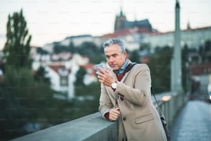 プラハ市のヴルタヴァ川のそばに立って、自分撮りをするスマートフォンを持つ成熟したハンサムな実業家。スペースをコピーします。