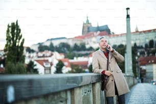 Mature businessman with smartphone standing on a bridge in city, making a phone call.