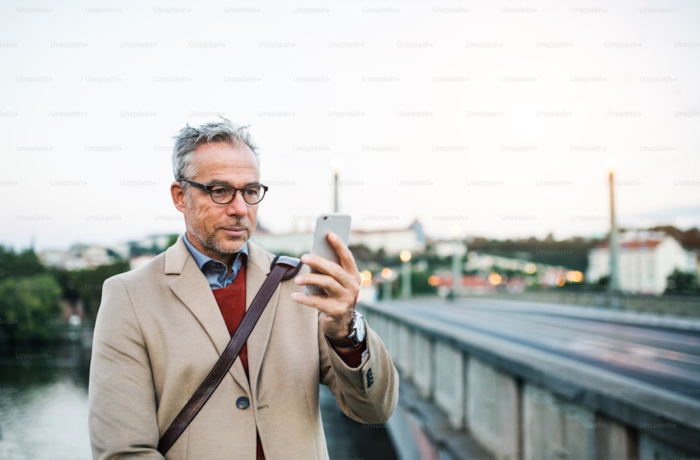 Hombre de negocios guapo maduro con teléfono inteligente parado junto al río Vltava en la ciudad de Praga, tomándose selfie. Espacio de copia.