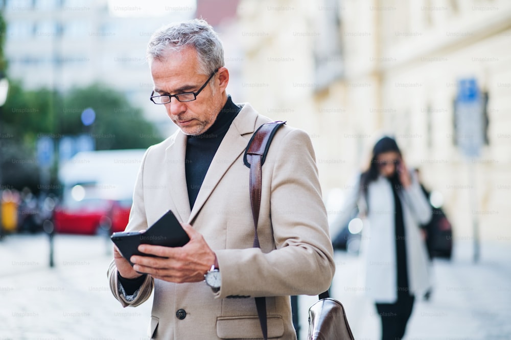 Hombre de negocios maduro parado en una calle de la ciudad, usando un teléfono inteligente. Espacio de copia.
