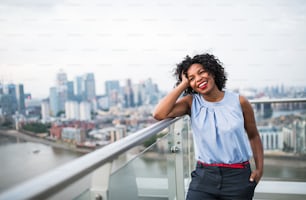 A portrait of a laughing black woman standing on a terrace in London. Copy space.