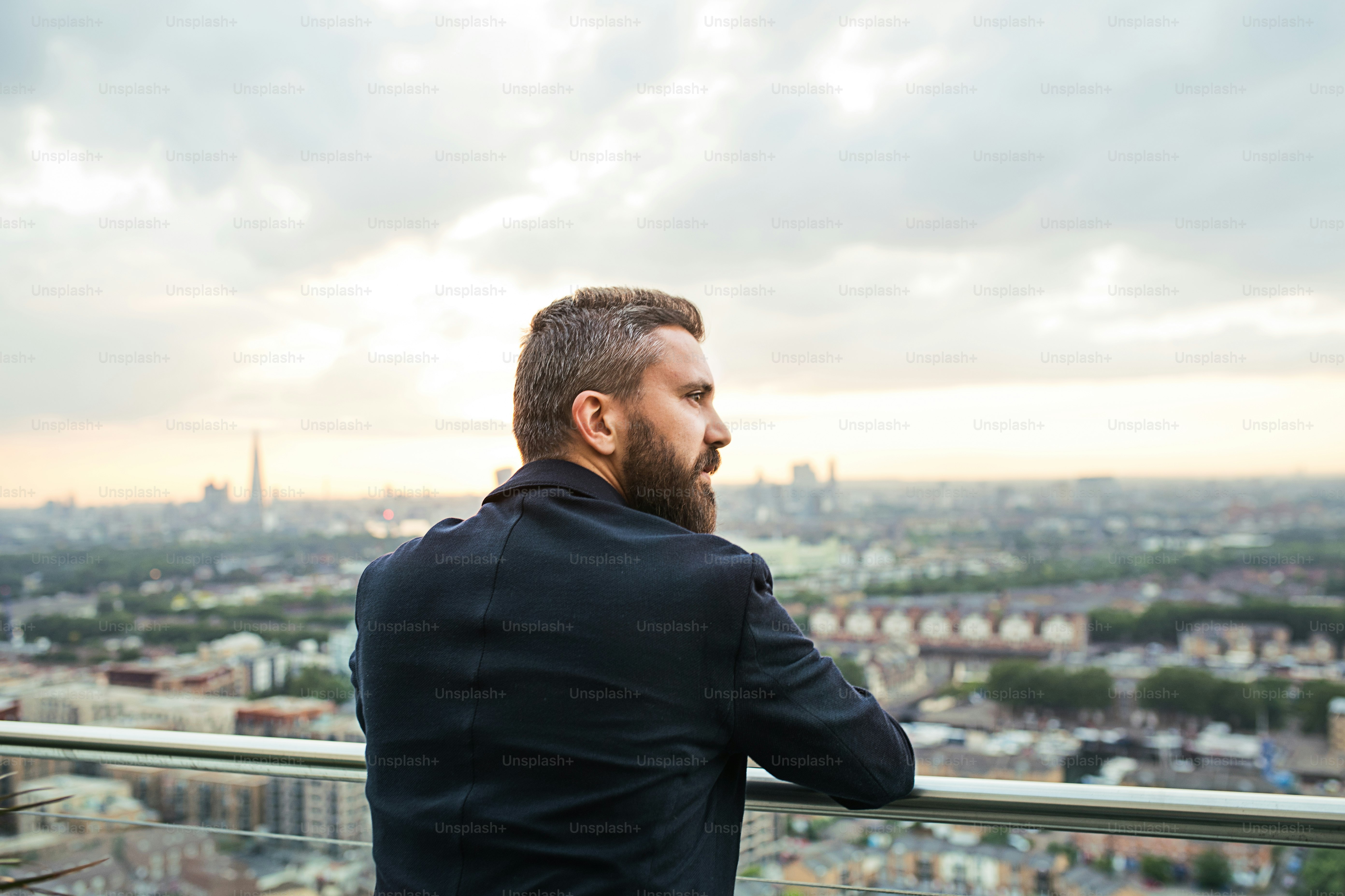 Una vista trasera de un hombre de negocios hipster de pie contra el panorama de la vista de Londres.